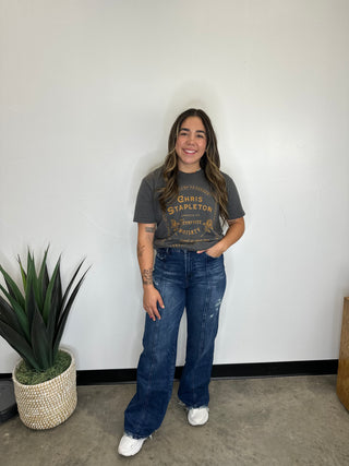 Girl with brown hair wearing dark wash jeans and t-shirt.  Jeans have seam down front of legs and light distressing on thigh. 